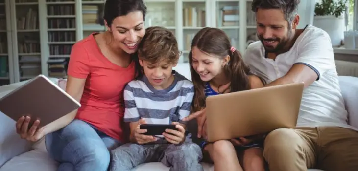 family of 4 being on a laptop, a tablet and a cellphone